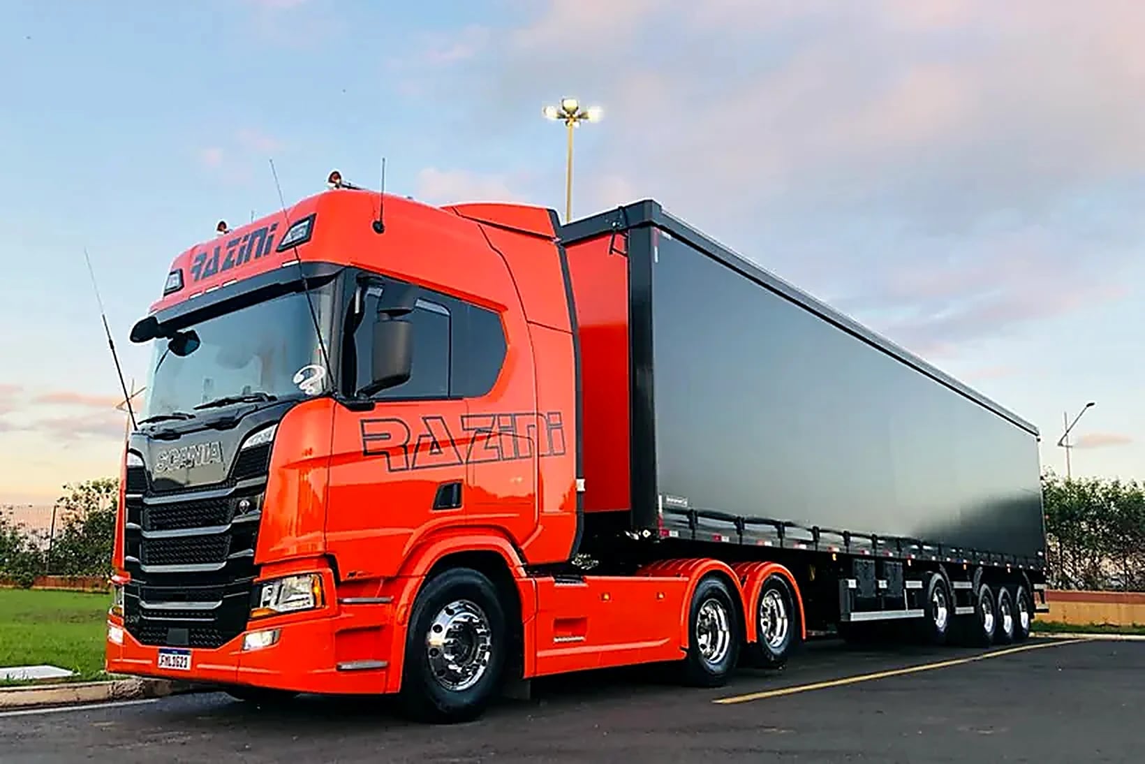 Scania laranja da Razini Transportes com carreta sider ao entardecer