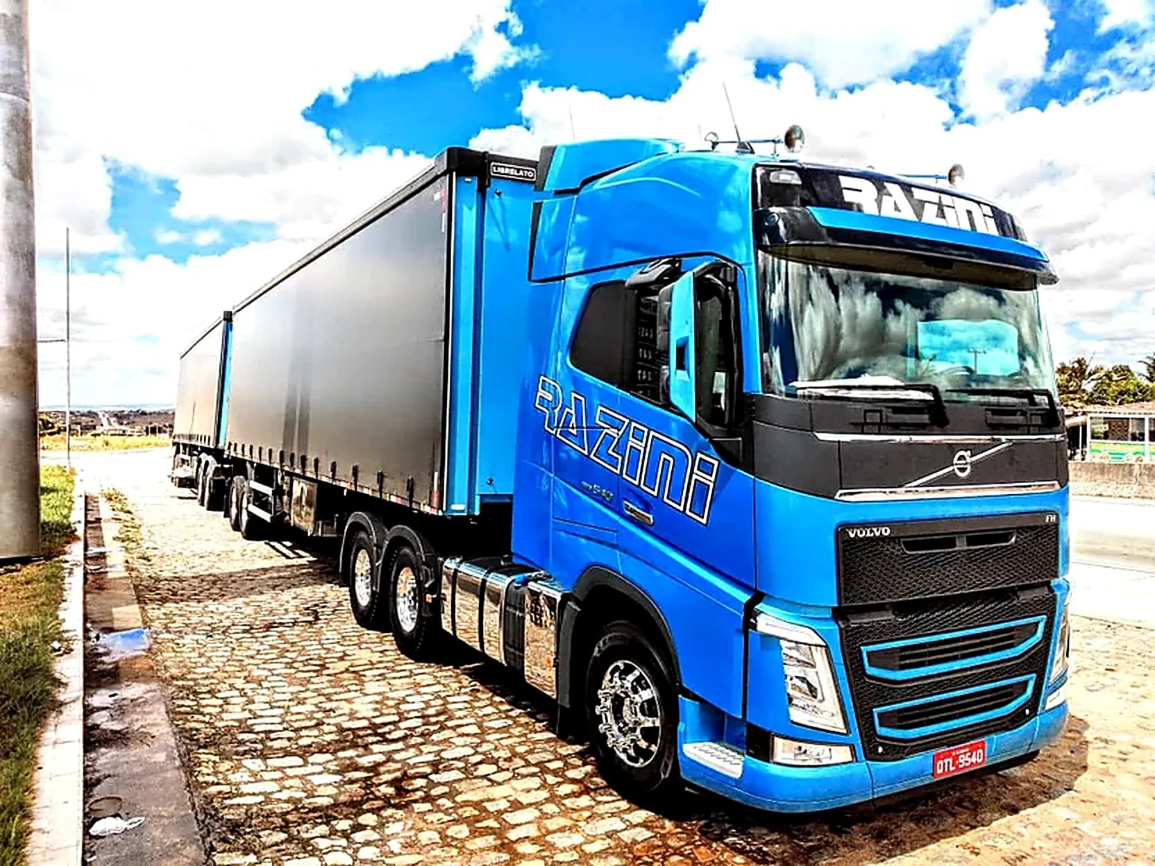 Volvo FH azul da Razini engatado, visto de frente em pátio de paralelepípedos